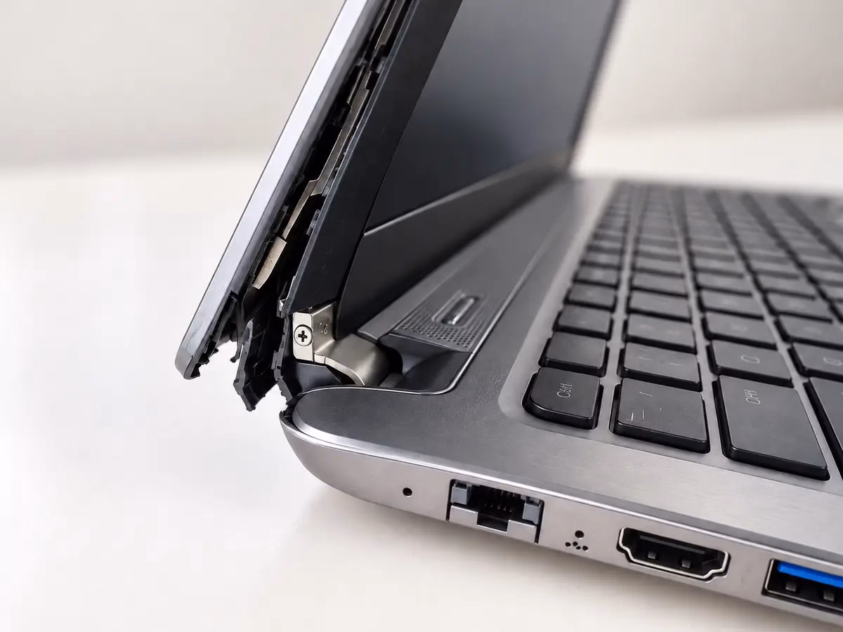 Close-up of a Windows business laptop with a broken hinge, separated screen bezel, and damaged lower case.