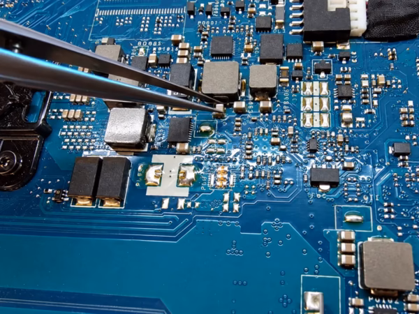 Precision tweezers point to a small component on a laptop motherboard during component-level repair.